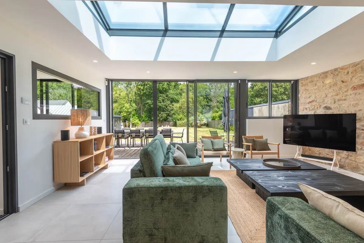 Wohnzimmer mit grünen Samtsofas und Fensterfronten zum Garten